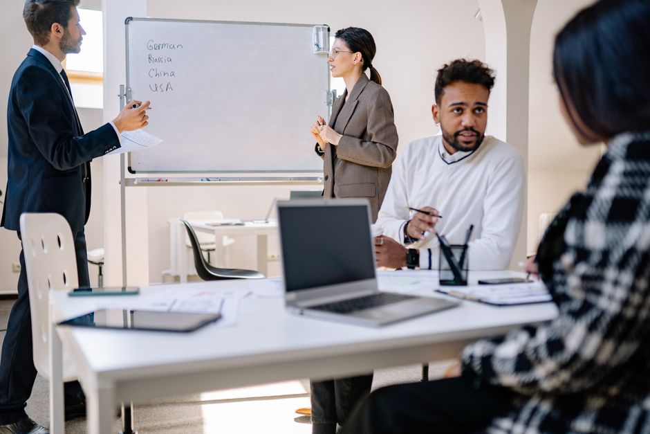 A diverse group of professionals engaged in a collaborative office meeting with laptops and a whiteboard.